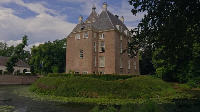 Castle Neerijnen in Holland, surrounded by its historic moat and lush greenery under a clear blue summer sky.