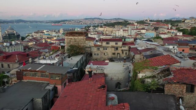 High aerial drone shot over old Istanbul red tile rooftops overlooking mosques, the Golden Horn waterway, Galata Bridge, and the modern city skyline during dusk twilight in Turkey.