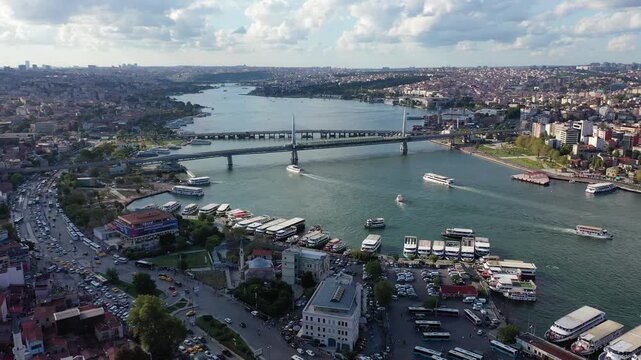 Wide aerial drone shot of the busy Eminonu bus and ferry terminals along the Golden Horn, with traffic flowing along coastal roads and bridges stretching across the water in Istanbul, Turkey.