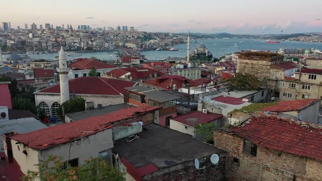 High aerial drone shot over old Istanbul red tile rooftops overlooking mosques, the Golden Horn waterway, Galata Bridge, and the modern city skyline during dusk twilight in Turkey.