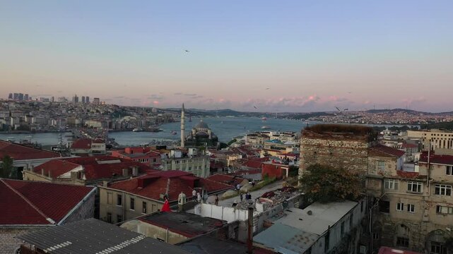 High aerial drone shot over old Istanbul red tile rooftops overlooking mosques, the Golden Horn waterway, Galata Bridge, and the modern city skyline during dusk twilight in Turkey.