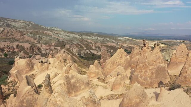 Wide aerial drone view of iconic fairy chimney rock formations and conical spires scattered across the rugged desert landscape of Devrent Valley, Cappadocia, Nevsehir, Turkey.