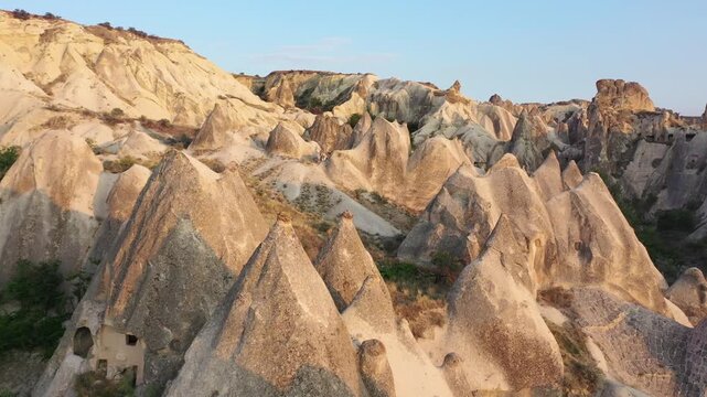Panoramic aerial drone view of white rock formations, conical fairy chimneys, and flat-topped tuff mountains in Rose Valley, Cappadocia, Nevsehir, Turkey under a clear blue sky.