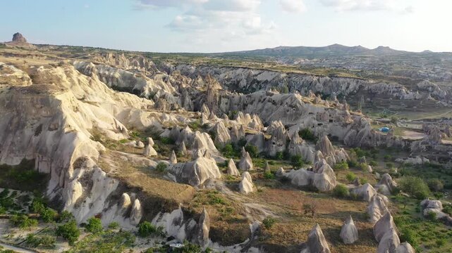 Panoramic aerial drone view of white rock formations, conical fairy chimneys, and flat-topped tuff mountains in Rose Valley, Cappadocia, Nevsehir, Turkey under a clear blue sky.