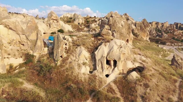 Panoramic aerial drone view of white rock formations, conical fairy chimneys, and flat-topped tuff mountains in Rose Valley, Cappadocia, Nevsehir, Turkey under a clear blue sky.