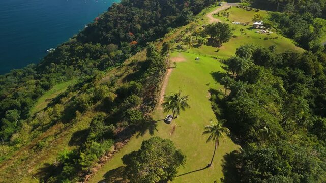 Aerial tilt up reveals Top of the World lookout on Mount Dillon above Tobago with panoramic view of Castara Bay coastline and rainforest ridge