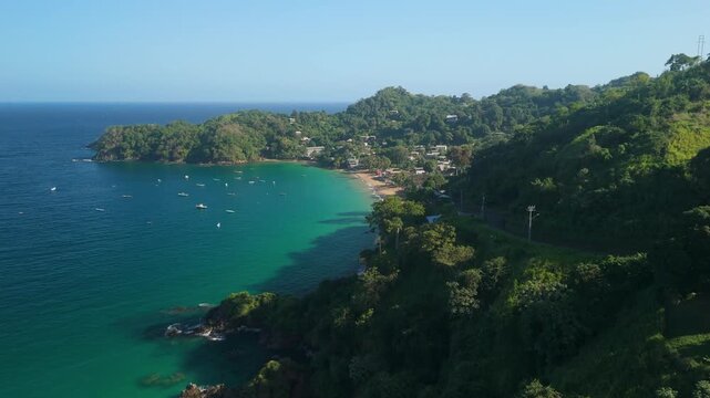 Aerial forward flight along Castara Bay Tobago revealing turquoise water sandy beach boats and green hills