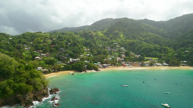 Aerial orbit Castara Bay Tobago showing dual crescent beach fishing boats hillside village and Main Ridge mountains