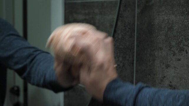 Male hand vigorously wipes a mirror with a damp cloth, demonstrating rapid movements, a clenched cloth, visible blurring, and the practical actions of cleaning a house with hands