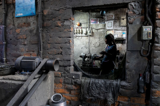 Dhaka, Bangladesh - 04 September 2024: View of a labourer working in a dimly lit aluminium factory with brick walls and industrial machinery.