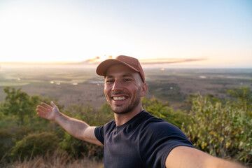 Fototapeta premium Man taking selfie during sunset on mountain enjoying freedom and adventure looking at camera and smiling