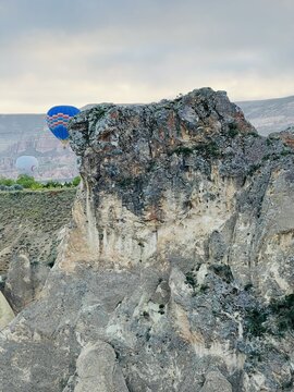Turkey - 11 August 2026: View of the unique volcanic rock formations of Cappadocia, with colorful hot air balloons floating in the distance under a cloudy sky.