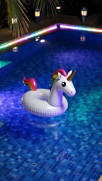 Illuminated swimming pool at night with inflatable unicorn float toy in clear water