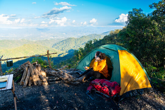 Asian woman listening to music with headphones and using smartphone mobile app while camping on the mountain. People enjoy outdoor active lifestyle nature therapy and wellness relaxing forest bathing