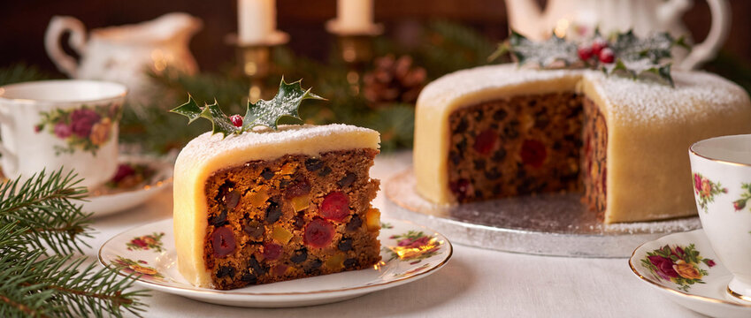 Traditional Christmas fruit cake slice with marzipan topping and holly garnish on festive table.