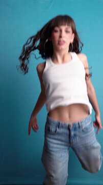 Energetic young woman dancing on a turquoise background