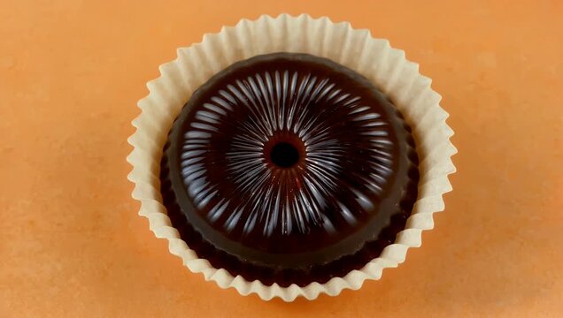 A round honey candy spinning inside a fluted paper wrapper against a vibrant orange backdrop highlighting sweet treats and commercial candy packaging