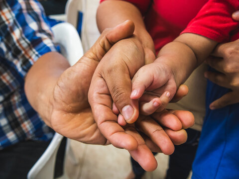 Close-up of an adult gently holding a baby's hand, capturing a tender moment of connection, care, affection, protection, family and childhood. The image focuses on the interaction between adult and ch