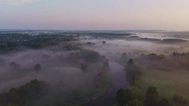 Aerial view of a misty river curving through forest under a pastel dawn sky