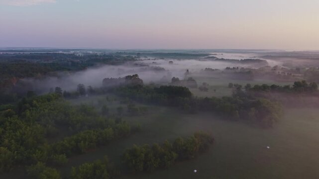 Aerial view of trees and meadows rising through soft morning fog under a pastel twilight sky near Wkra river Mazovia