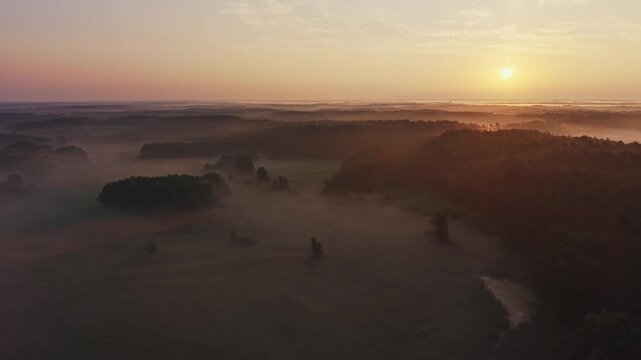 Aerial view of the sun rising over misty meadows and forest clusters with a small pond near Wkra river in Mazovia