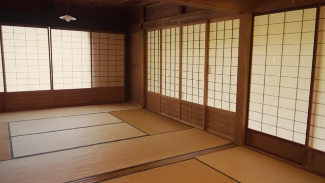 Empty and peaceful Japanese style room with traditional tatami mat flooring, fusuma and shoji paper screen sliding doors. Warm sunlight gently illuminates the serene and historic interior