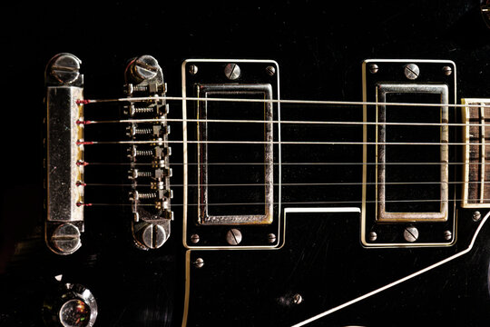 Electric guitar close-up featuring glossy black finish, metallic bridge, six-string setup, two humbucking pickups, taut strings, studio lighting, high contrast