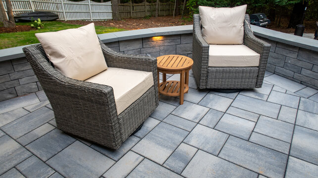 Outdoor Patio Seating Area With Wicker Swivel Chairs Wooden Side Table And Stone Retaining Wall