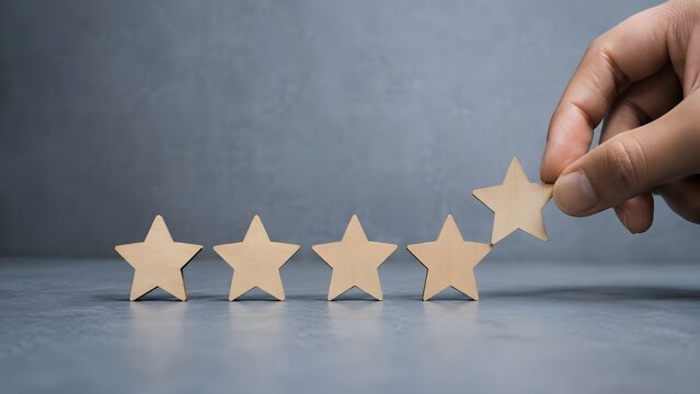 Hand placing fifth wooden star in a row on grey background symbolizing top quality excellent performance customer satisfaction and perfect rating review