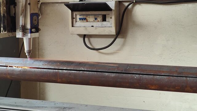 Laser cutting machine processing rusty metal pipe with flying sparks