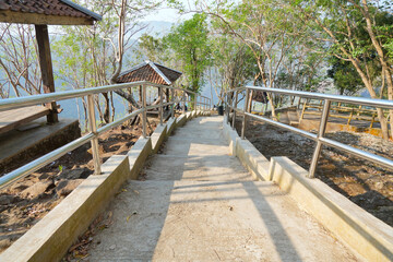 Obraz premium Concrete stairs with stainless steel handrails leading down a forested hill with wooden gazebos surrounded by lush trees in Yogyakarta, Indonesia. A scenic park trail for tourists.