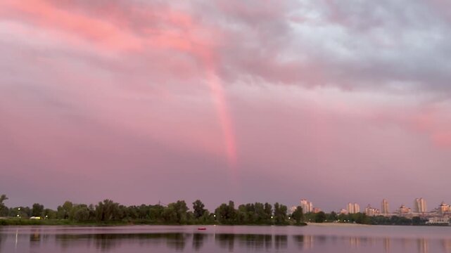 Smooth tilt up over calm water toward rainbow in pink sunset sky