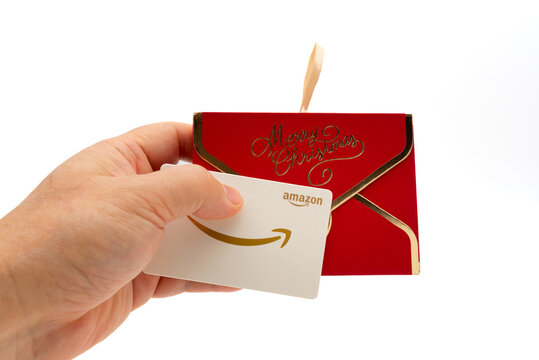 Fuji, Shizuoka, Japan - November 14, 2024: A hand holding an Amazon gift card in front of a red decorative "Merry Christmas" envelope on a white background.