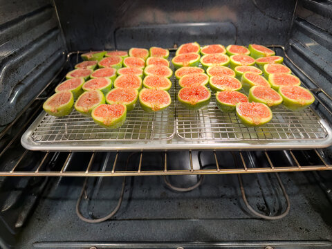 Sliced fresh raw organic desert king figs ready to be dehydrated for future storage on dry racks and metal baking sheet within oven