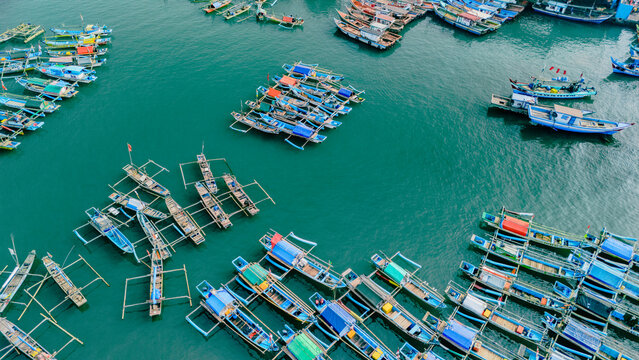 Aerial view of colorful wooden fishing boats and traditional outriggers moored in the turquoise waters of the harbor in Palabuhanratu, Indonesia.