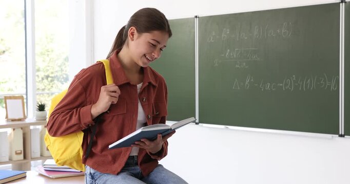 Teenage girl with book and backpack in classroom