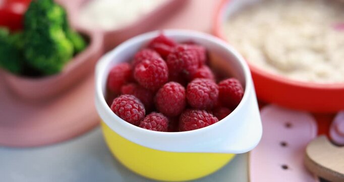 Baby tableware. Cup with fresh raspberries on grey table, closeup. Camera moving forward