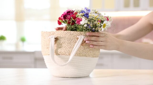 Woman with wildflowers in bag at white table indoors, closeup
