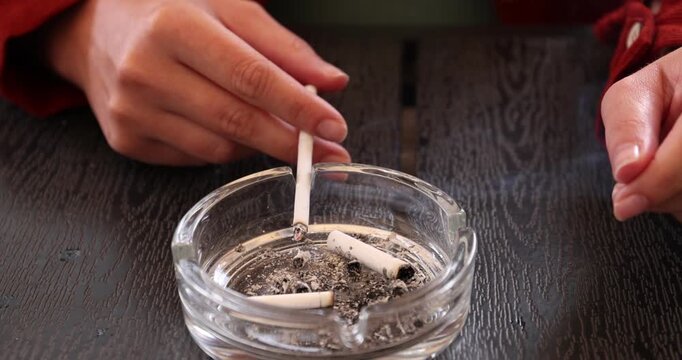 Woman flicking ash from cigarette into ashtray at wooden table, closeup