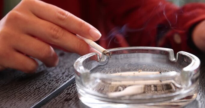 Woman flicking ash from cigarette into ashtray at wooden table, closeup
