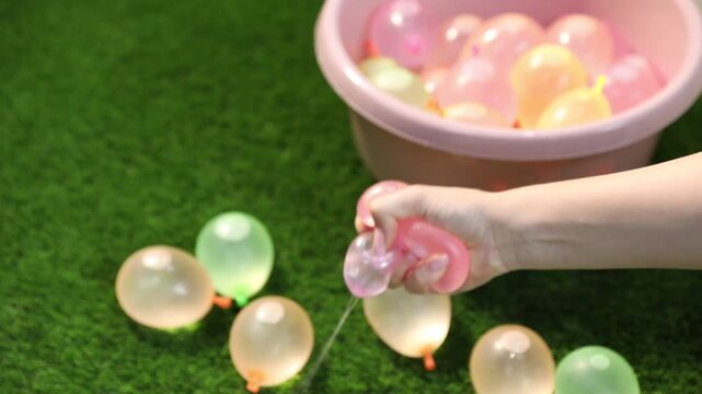 Woman taking water balloon from basin and squeezing it on green grass, closeup