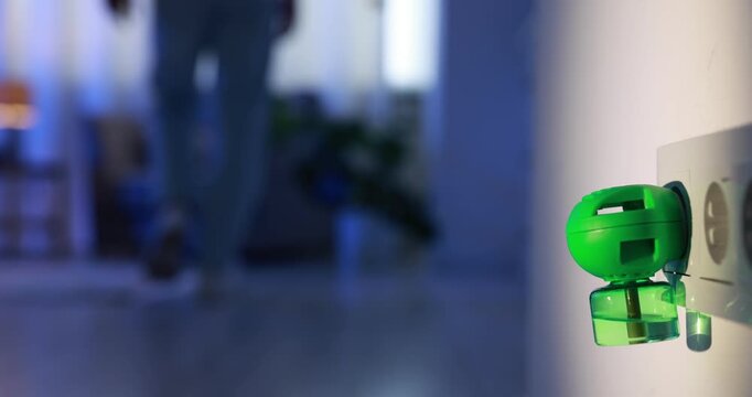 Man plugging in electric mosquito repeller with liquid refill at home at night, closeup