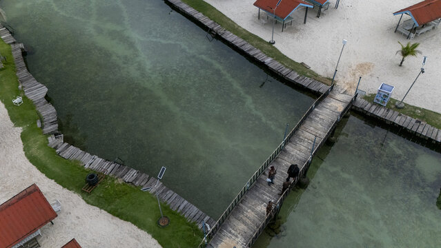 Aerial view of McCarthy beach featuring a wooden pier extending over clear green water, sandy shores, and small shelters in Urhuoka, Delta, Nigeria.