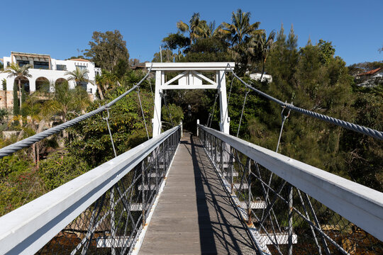 Old Wood Suspension Walking Bridge over water in bush setting on sunny day with blue sky. Wide view of walkway in sun
