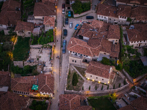 Aerial view of historic Ottoman-style houses with terracotta rooftops, narrow cobblestone streets, and illuminated stone buildings at dusk in Berat, Berat County, Albania.