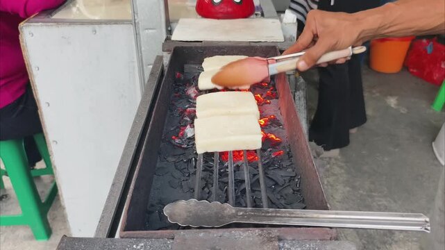 Street Vendor Placing Fresh White Uli Bakar Rice Cakes on Hot Charcoal Grill to Start Cooking