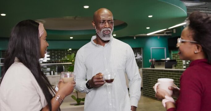African American coworkers moving mugs to senior man, clinking at office counter, celebrating win