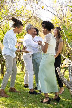 Diverse friends gathering on lawn under drape, in light attire, sharing pastries on tiered stand