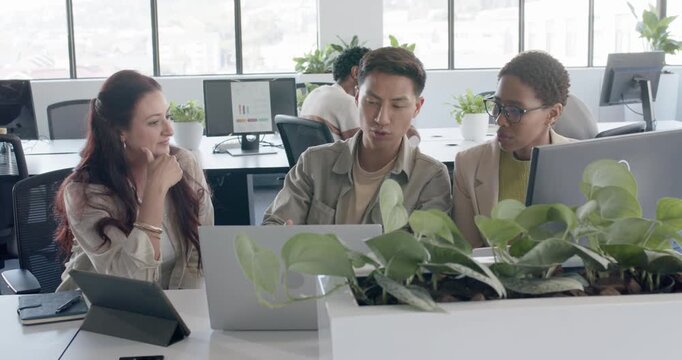 Diverse coworkers reviewing plan after man pointing at laptop while left woman referencing tablet