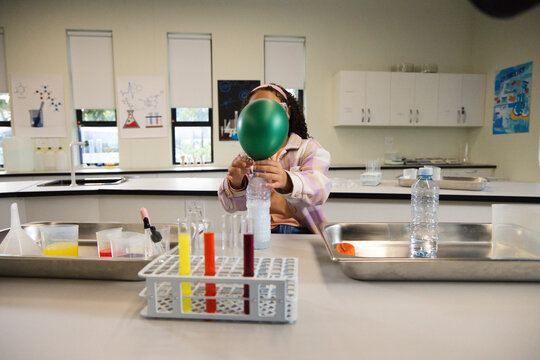African American youth sitting school lab holding green balloon on clear bottle near test tube rack